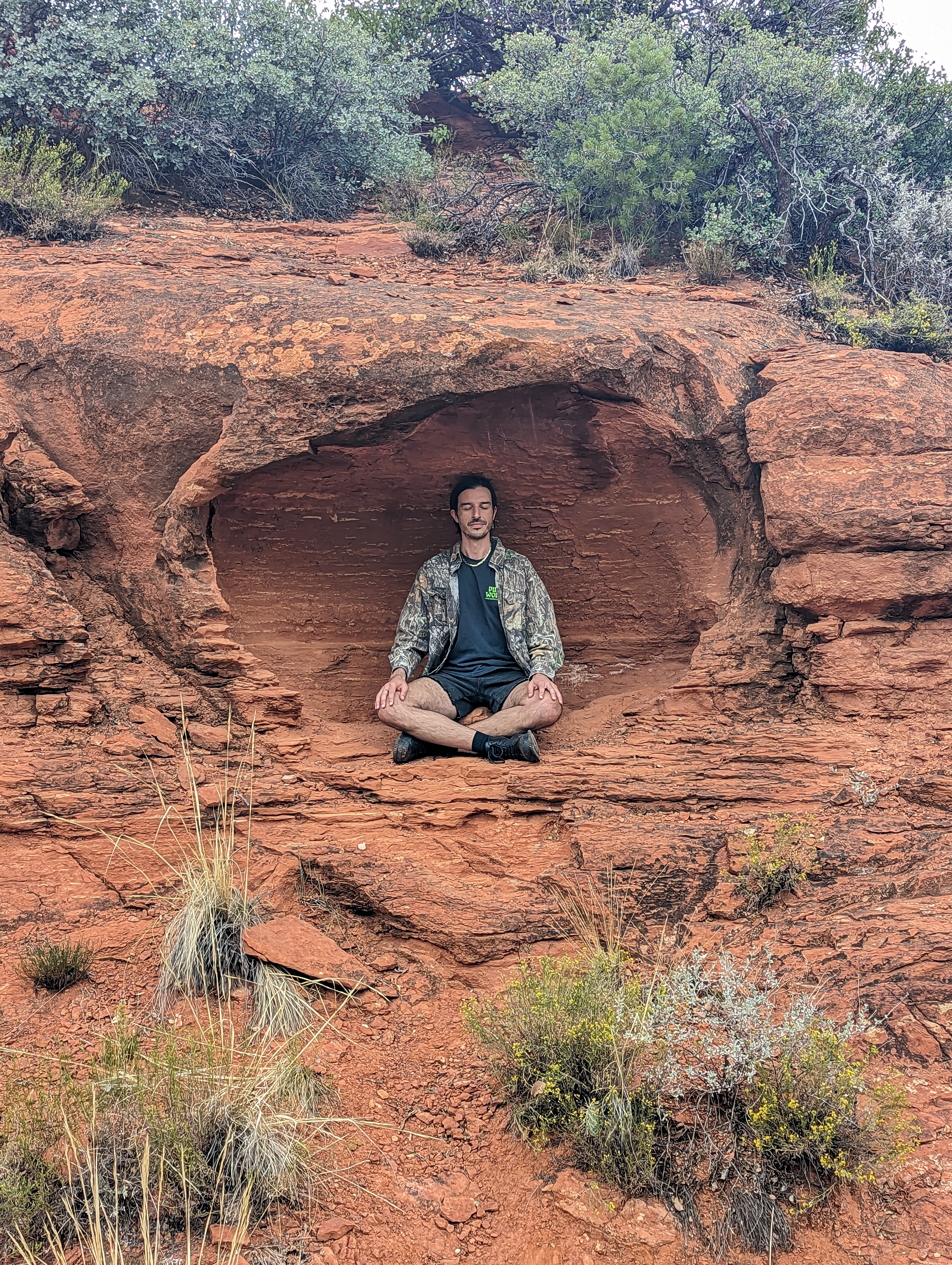 Savino meditating cross-legged inside a natural red rock cave in Sedona, Arizona